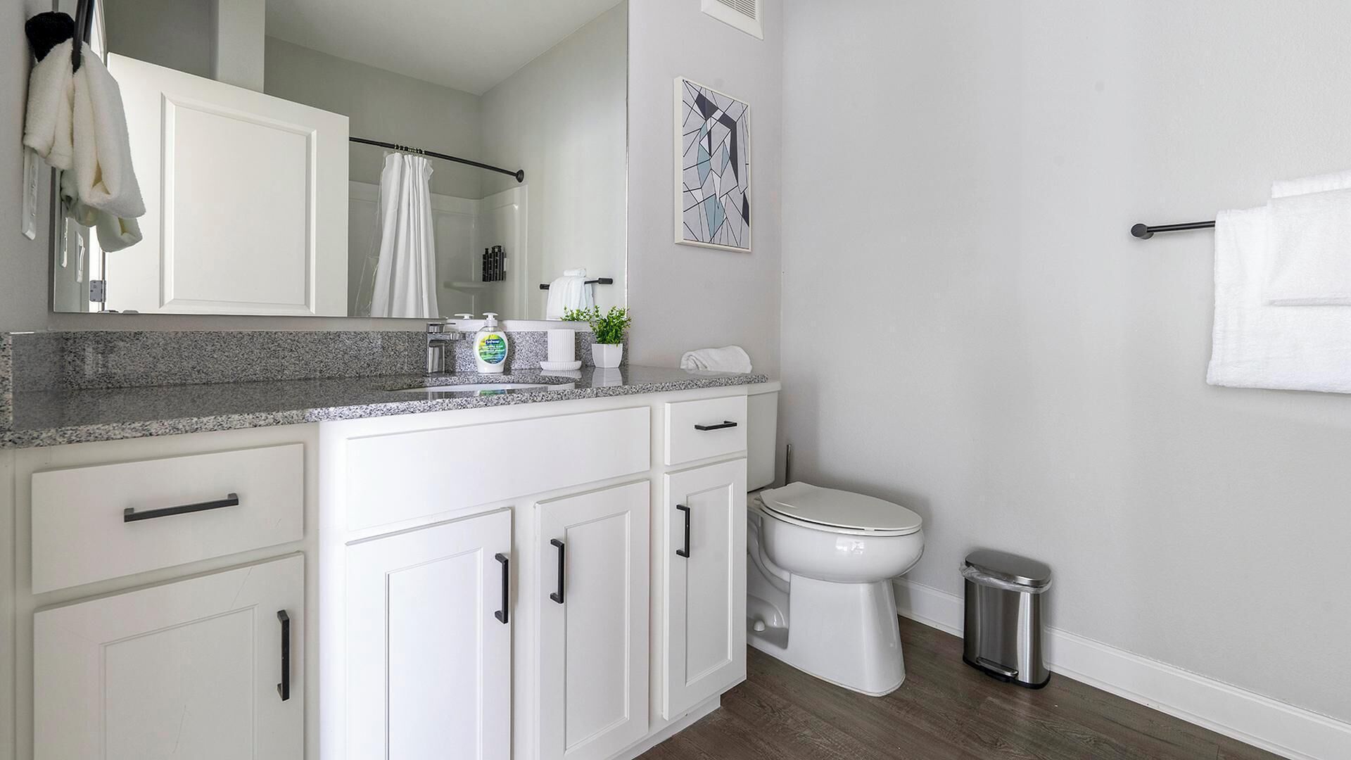 Une salle de bain moderne avec des meubles blancs, un comptoir en granit, des toilettes et une poubelle.