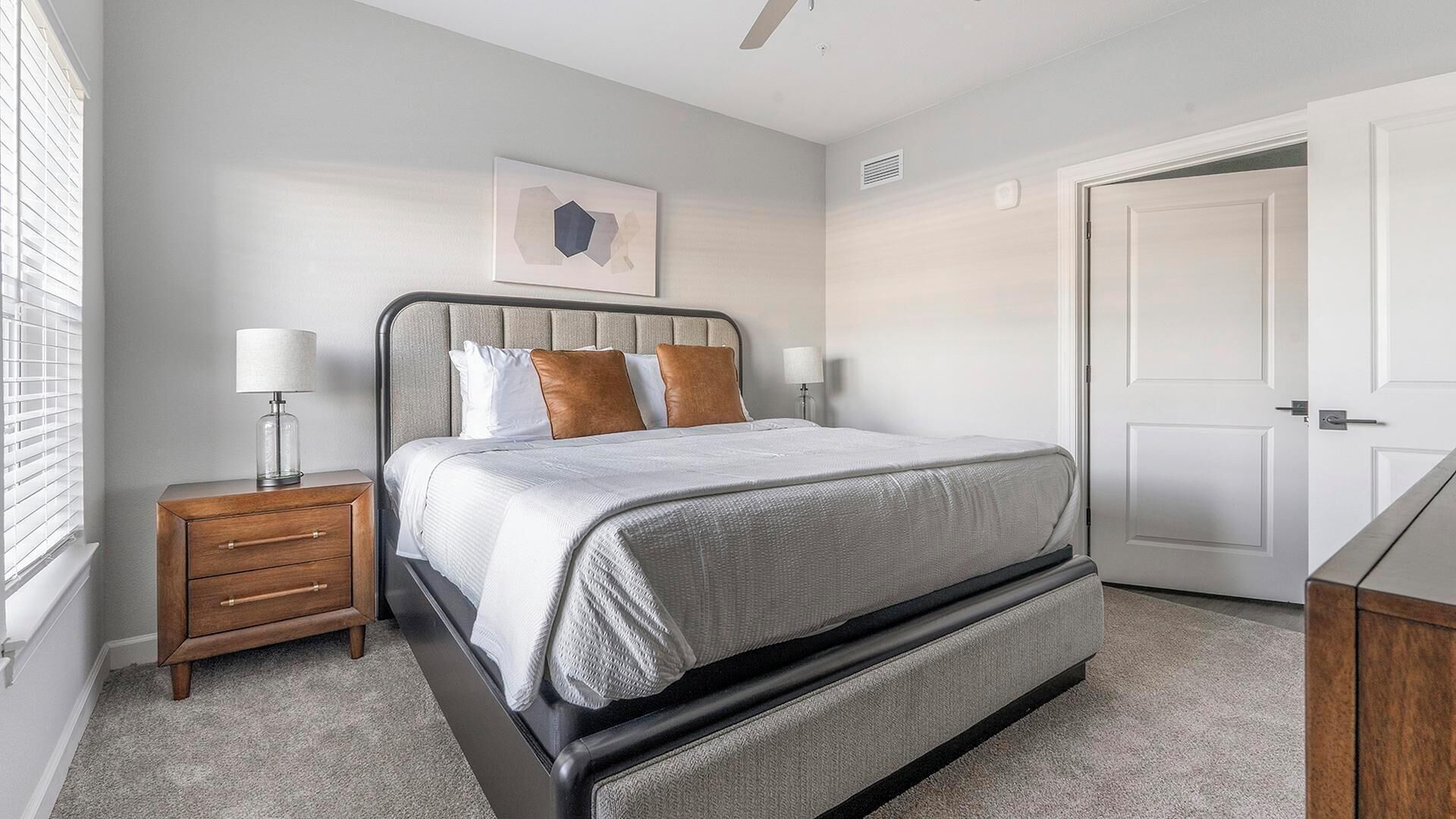 A bedroom with a bed, bedside tables, a nightstand, a door, and a wall-mounted artwork.