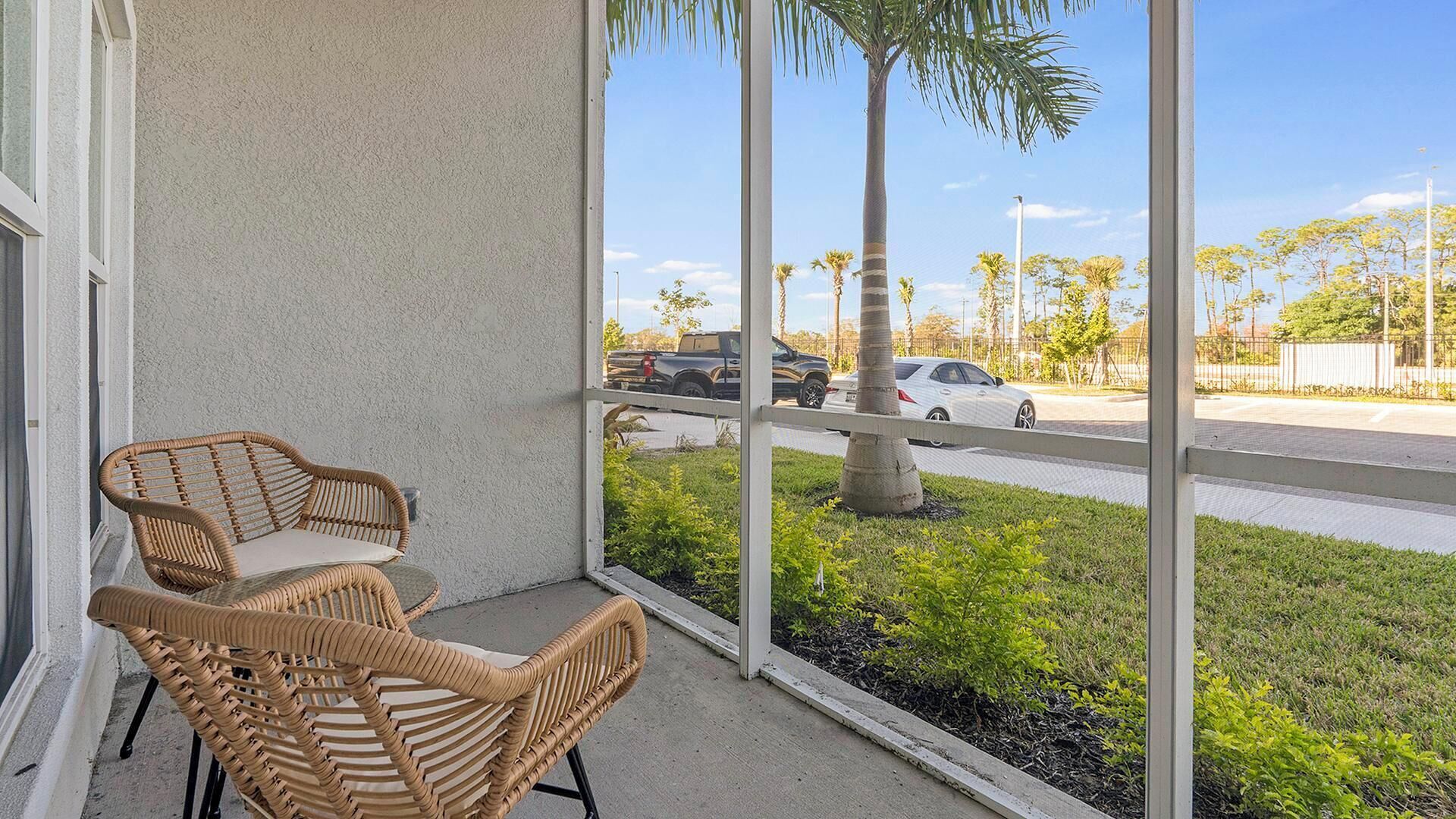 Een balkon met rieten stoelen en uitzicht op een straat met palmbomen en geparkeerde auto's.