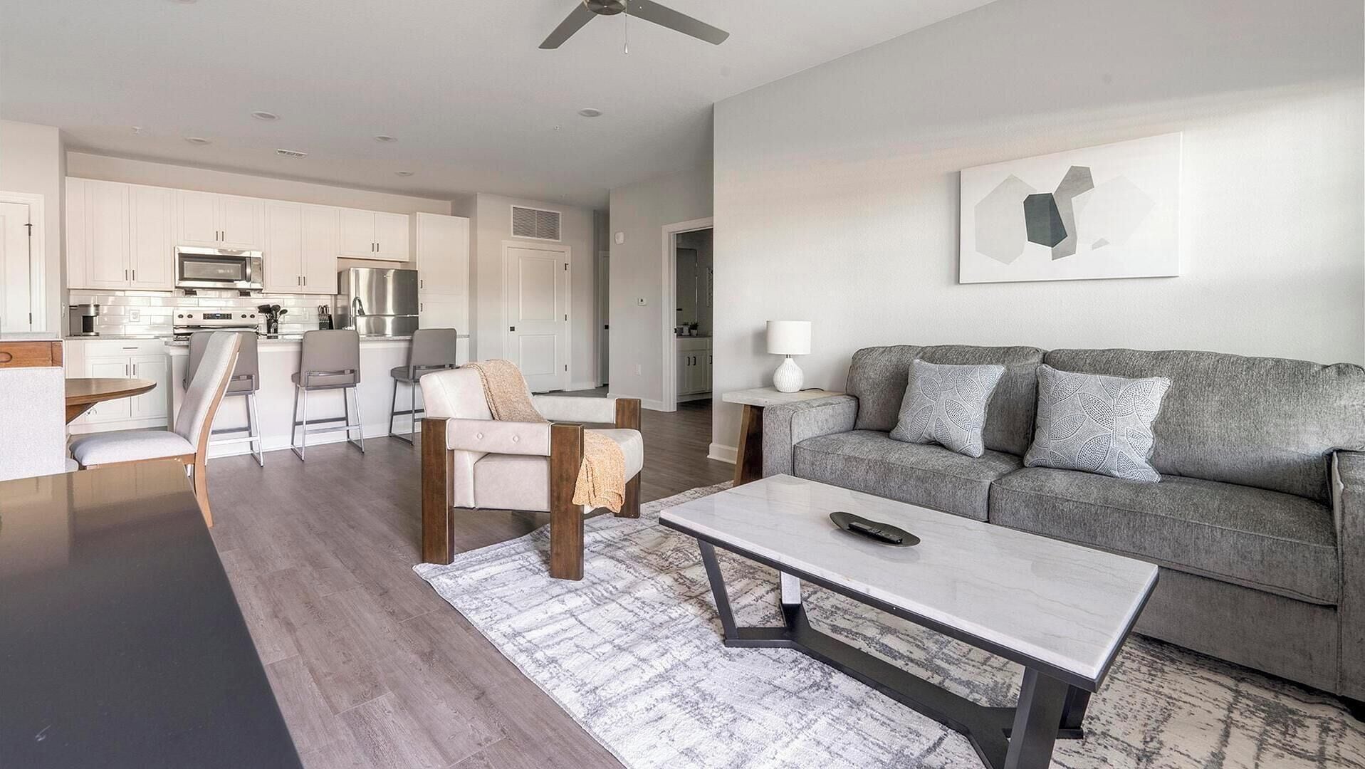 A modern living room with a grey sofa, a coffee table, and a dining area with a kitchen in the background.
