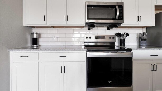 A modern kitchen with white cabinetry, a stainless steel microwave, a built-in oven, and a coffee maker. - Landing | Stylish 2BD, Pool (Tice)