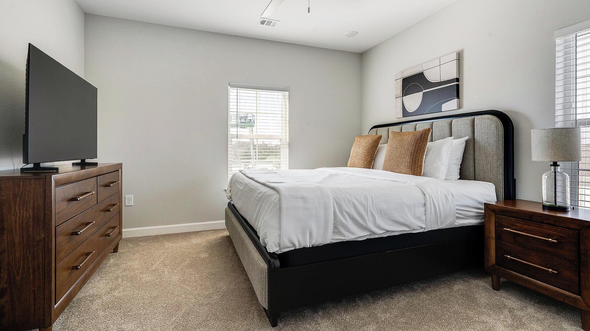 A bedroom with a bed, a dresser, a TV, and a window with blinds.