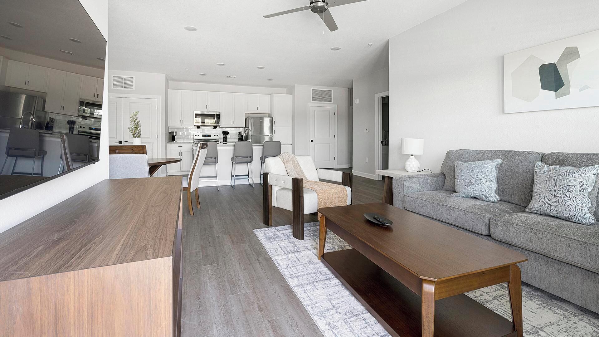 Una sala moderna con un sofá gris, una mesa de centro de madera y un comedor con sillas blancas y una mesa de madera.