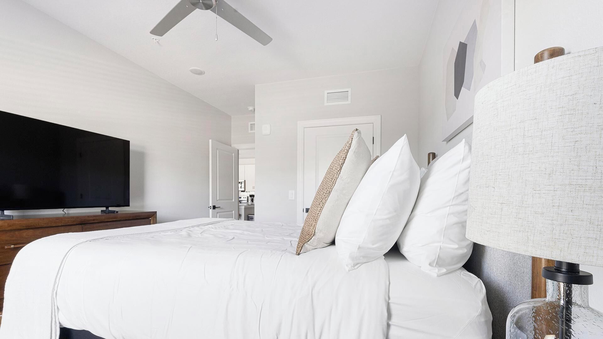 A modern bedroom with a large bed, a flat-screen TV, and a ceiling fan.