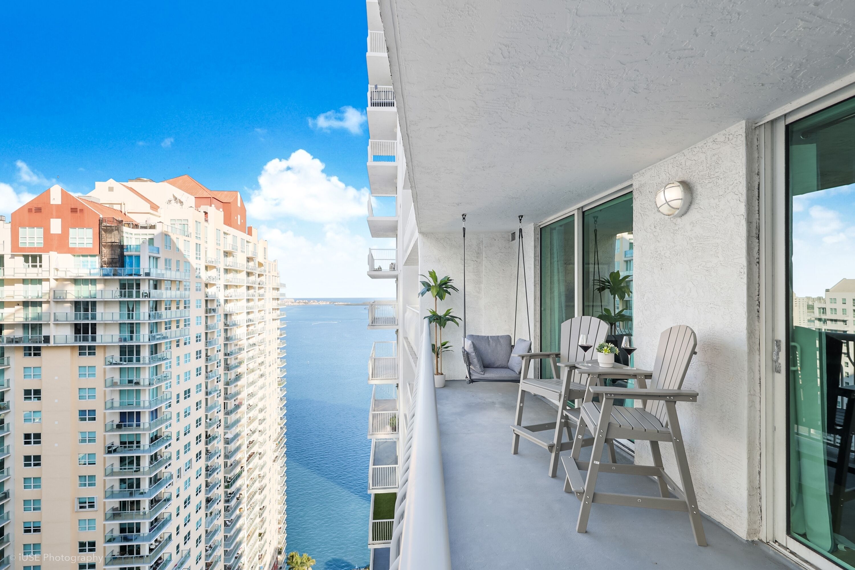 A balcony with a table and chairs, overlooking a body of water and high-rise buildings.