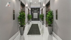 A modern hallway with a central rug, potted plants, and elevator doors. - Sky-High Luxury 1BR with Brickell City & Bay Views (Miami)