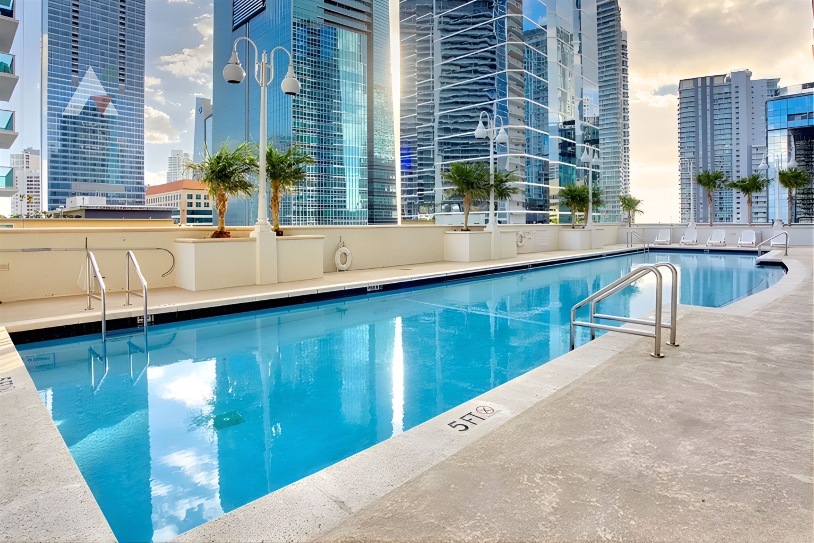 Una piscina con un indicador de profundidad de 1,5 metros, rodeada de palmeras y edificios modernos al fondo.
