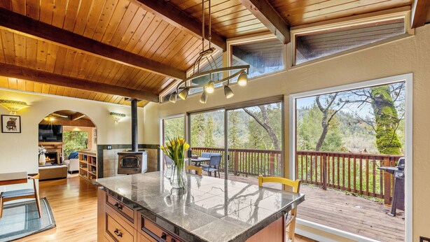 A spacious kitchen with a large island, wooden ceiling, and large windows offering a view of the deck.