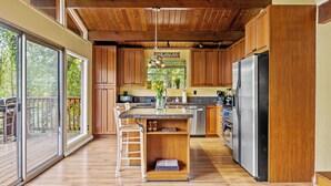 A spacious kitchen with wooden cabinets, a stainless steel refrigerator, and a large island with a sink.