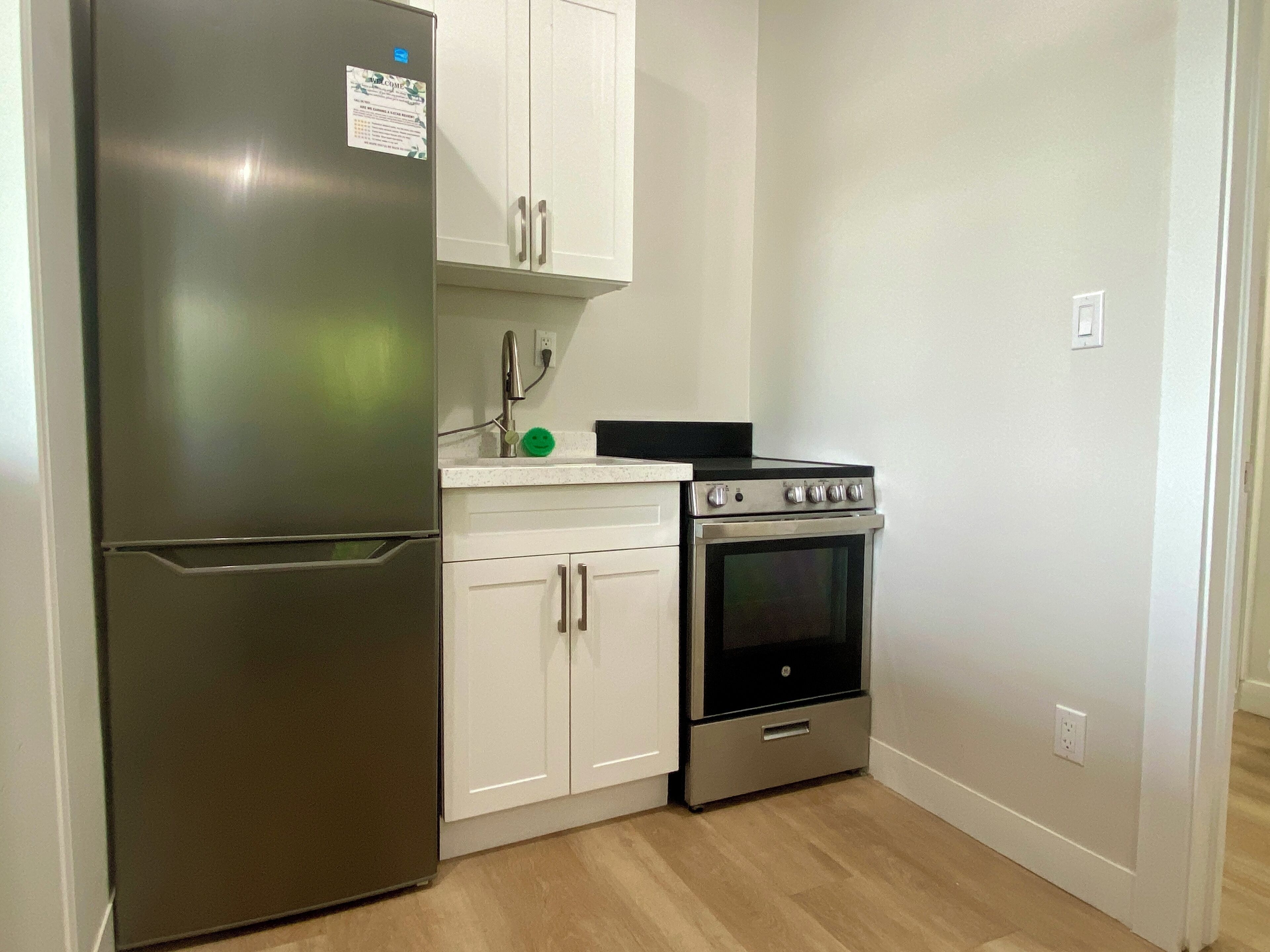 Una cocina compacta con refrigerador de acero inoxidable, horno integrado y armarios blancos.