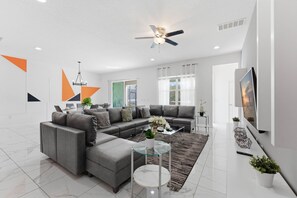 A modern living room with a sectional sofa, a glass coffee table, and a ceiling fan. - Chic Modern Escape, 12BR, Pool and Game Room (Kissimmee)