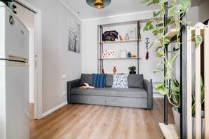 Een moderne woonkamer met een grijze bank, houten vloeren en een inbouwkast met diverse decoratieve objecten.