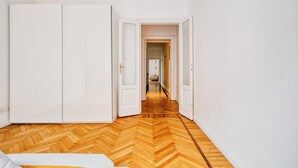 Ein Zimmer mit Holzboden im Fischgrätmuster, weißen Wänden und einem großen Kleiderschrank.