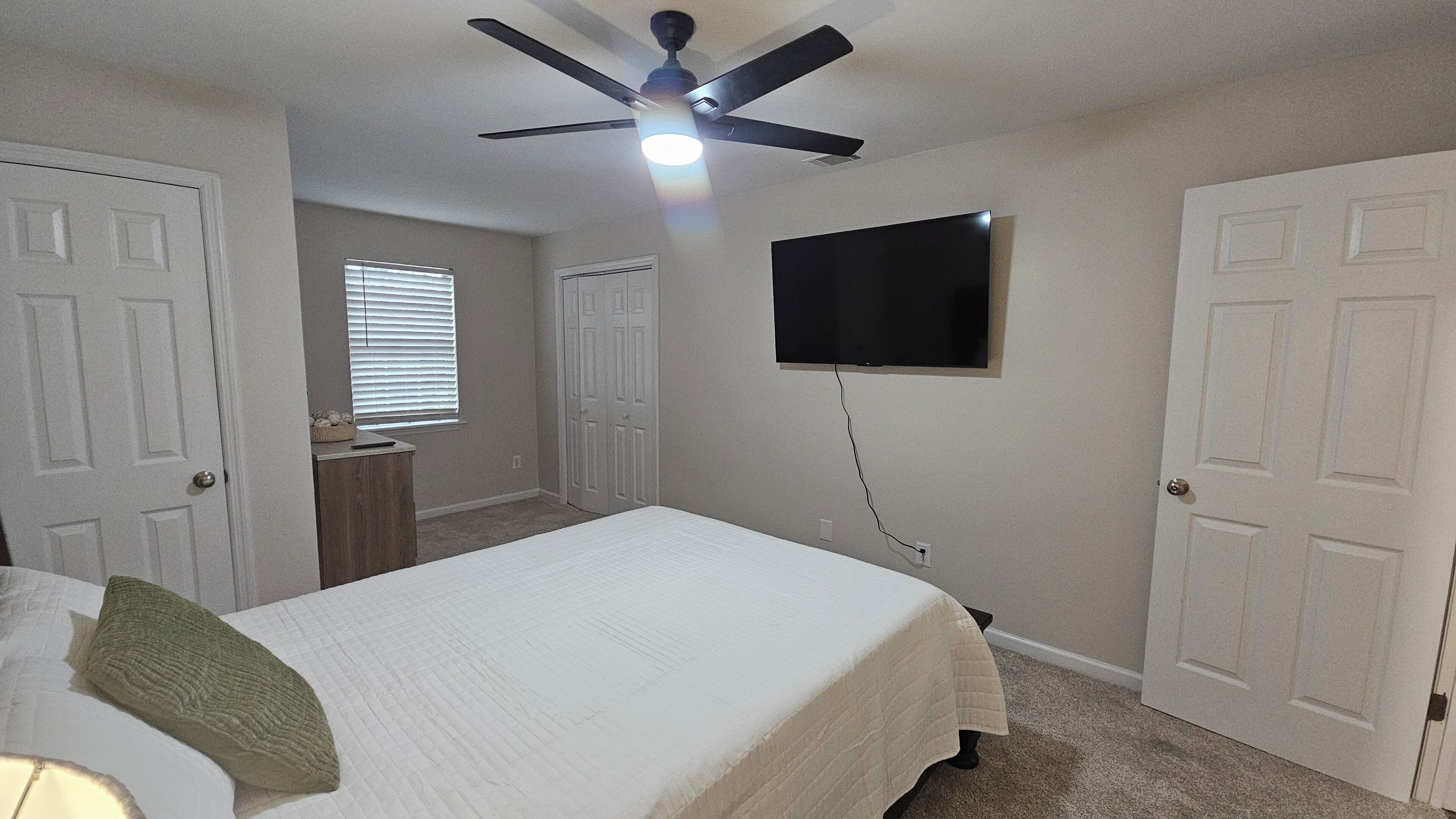 Une chambre à coucher avec un lit, un ventilateur de plafond, une télévision et une porte.