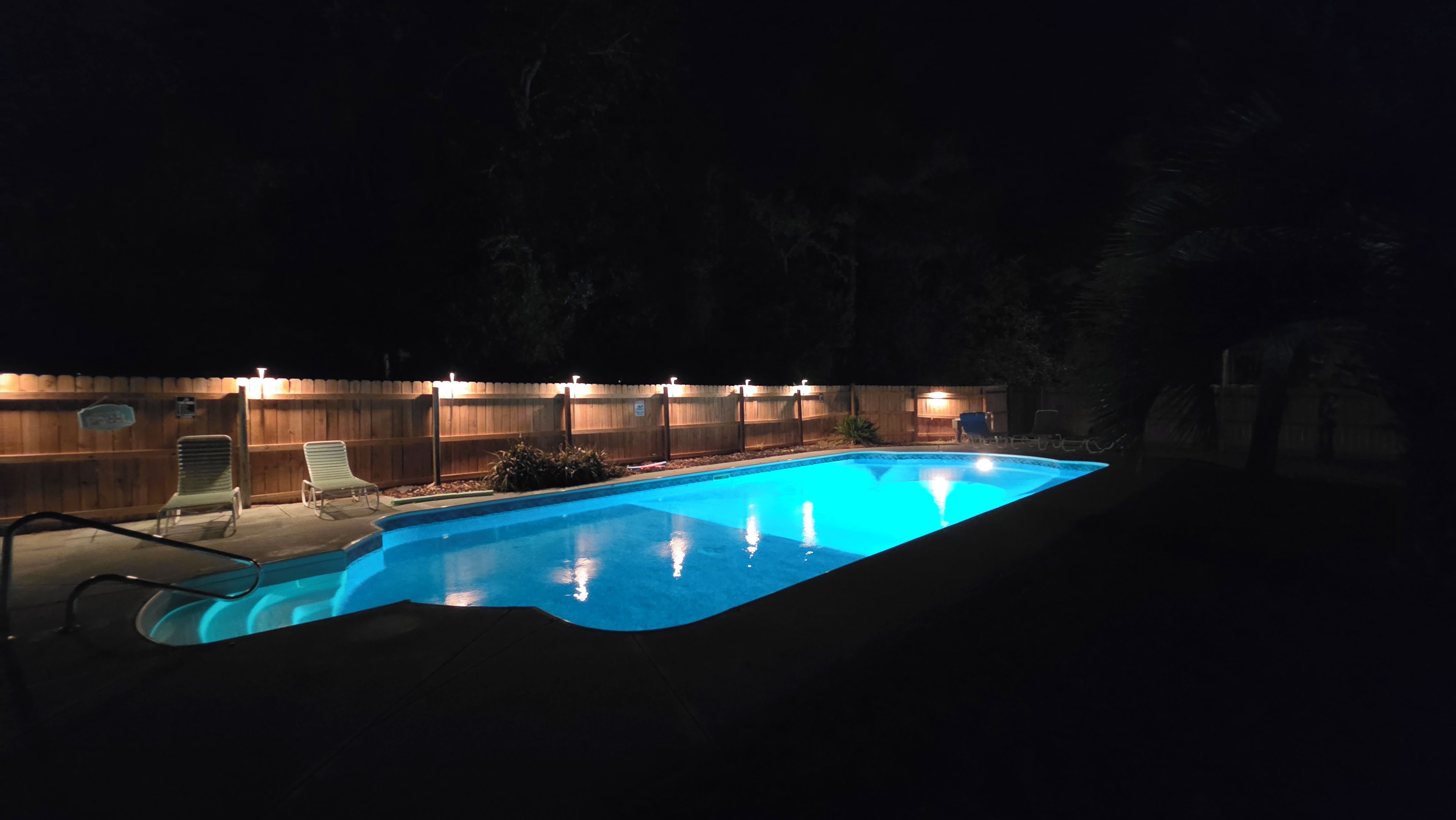 A swimming pool with a wooden deck, lounge chairs, and a wooden fence.