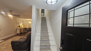A staircase with patterned carpet leading to a second floor, a dining area with a table and chairs, and a black door with a window.