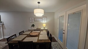 A dining room with a wooden table, chairs, a hanging light fixture, and wall-mounted artwork.