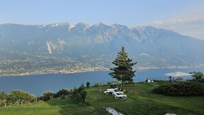 Eine Rasenfläche mit Liegestühlen, einem Baum und Blick auf einen See und Berge.