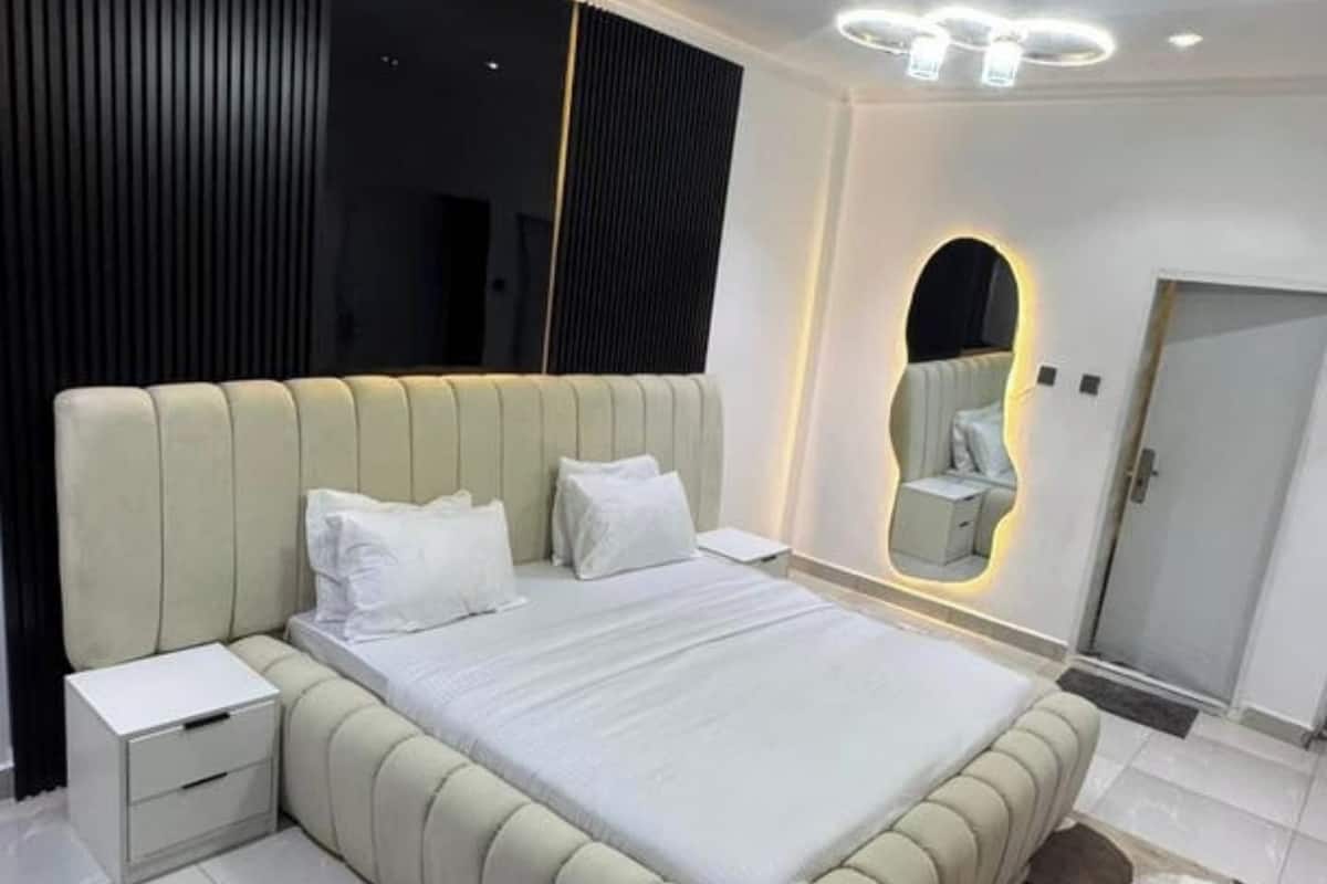 Une chambre à coucher moderne avec un grand lit, une table de chevet, un miroir et une porte.