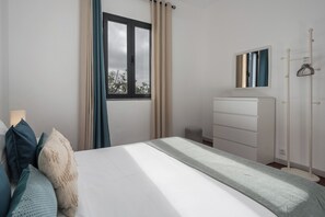 A bedroom with a bed, a dresser, a mirror, and a window with curtains. - Casa Maria Bela – 2-Bedroom with Terrace (Arco da Calheta)