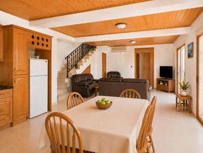 A spacious living area with a dining table, wooden cabinets, a sofa, and a staircase. - Villa Chrisandria - Three Bedroom Villa, Sleeps 6 (Argaka)