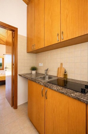 A kitchen with wooden cabinets, a granite countertop, a sink, and a small potted plant. - Villa Chrisandria - Three Bedroom Villa, Sleeps 6 (Argaka)