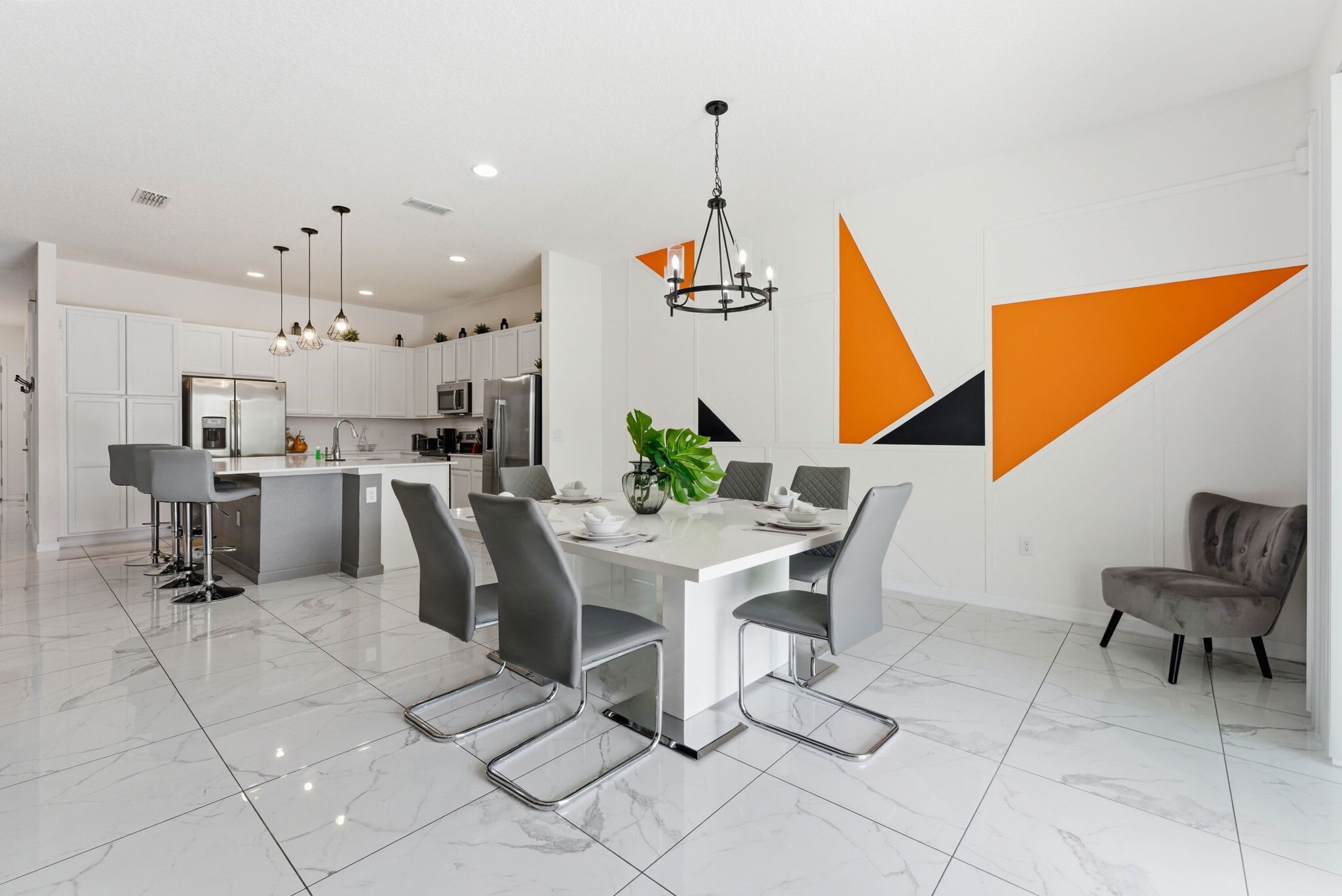 Una cocina moderna con armarios blancos, una isla central y un comedor con mesa blanca y sillas grises.