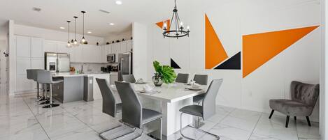 Una cocina moderna con armarios blancos, una isla central y un comedor con mesa blanca y sillas grises.