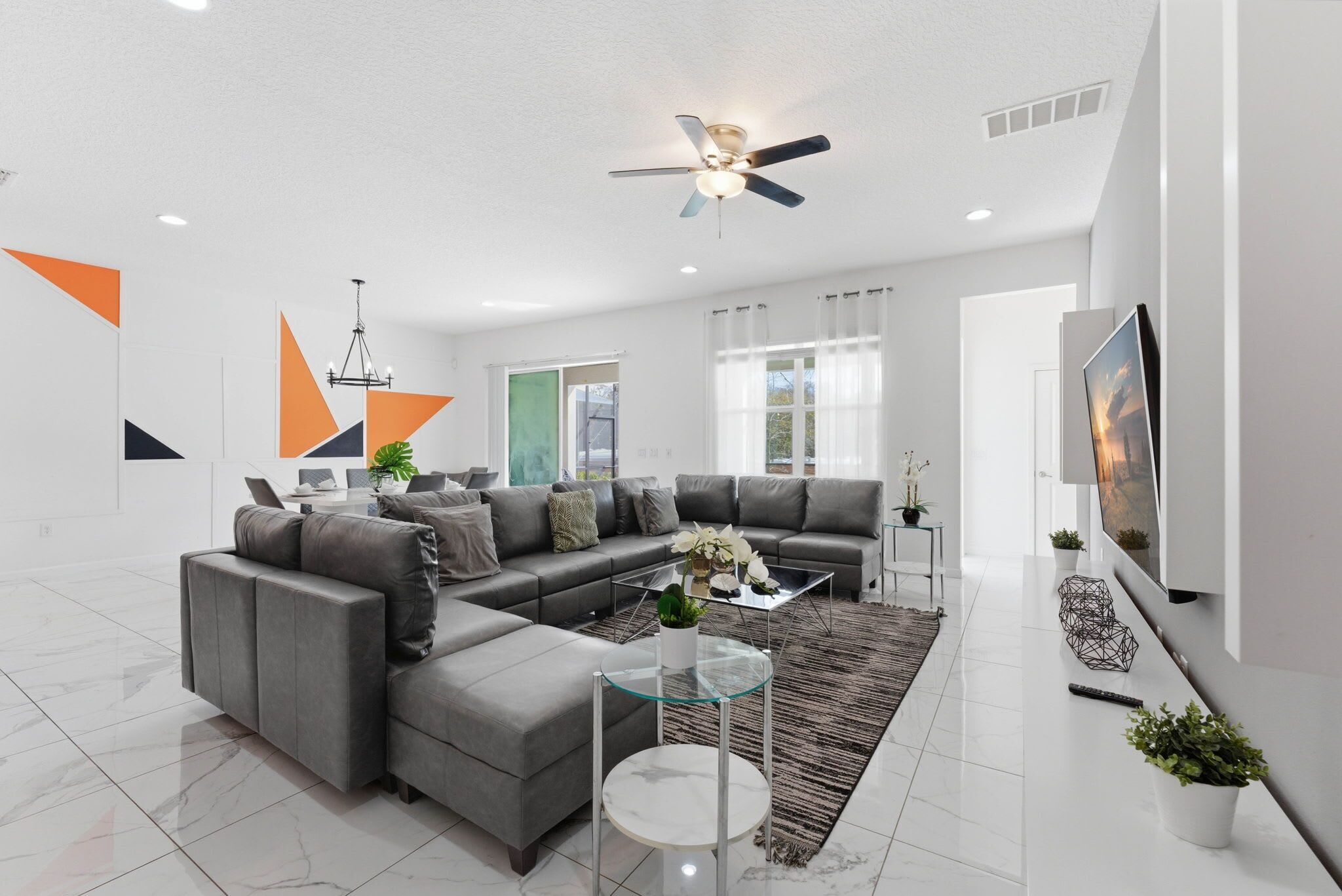 A modern living room with a sectional sofa, a glass coffee table, and a ceiling fan.