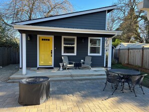 Une maison à deux étages avec une porte d’entrée jaune, un porche couvert et un patio aménagé avec du mobilier d’extérieur.