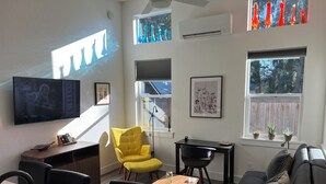 Una sala de estar moderna con un sillón amarillo, un sofá negro, una mesa de comedor y un televisor de pantalla plana montado en la pared.