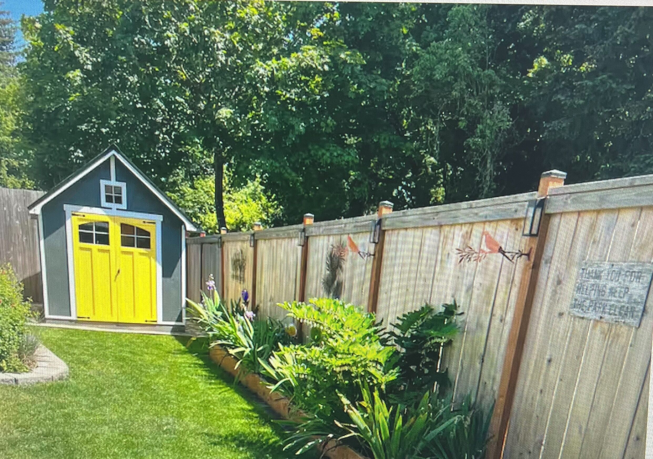 A fenced backyard with a small shed, a well-maintained lawn, and various plants.