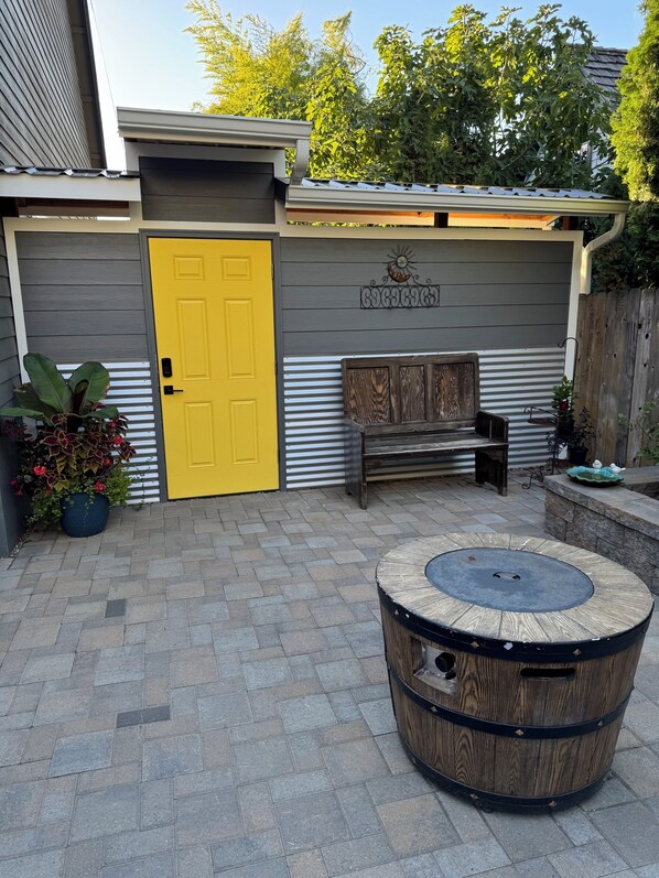 Un espace patio avec une porte jaune, un banc en bois et un foyer de forme cylindrique.