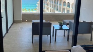 Un balcón con vistas al océano y un edificio de hotel. Hay un sofá y una mesita con una planta.