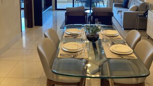Un comedor moderno con una mesa de vidrio preparada para cuatro personas, rodeada de sillas de cuero. Un ventanal ofrece vistas al exterior.