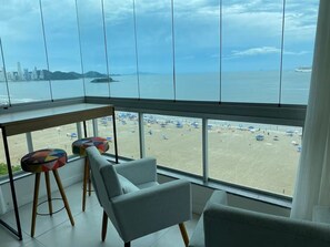 A room with a large window overlooking a beach and city skyline. - Beautiful beachfront apartment in Balneário Camboriú. Cozy and with a stunning view. (Balneário Camboriú)