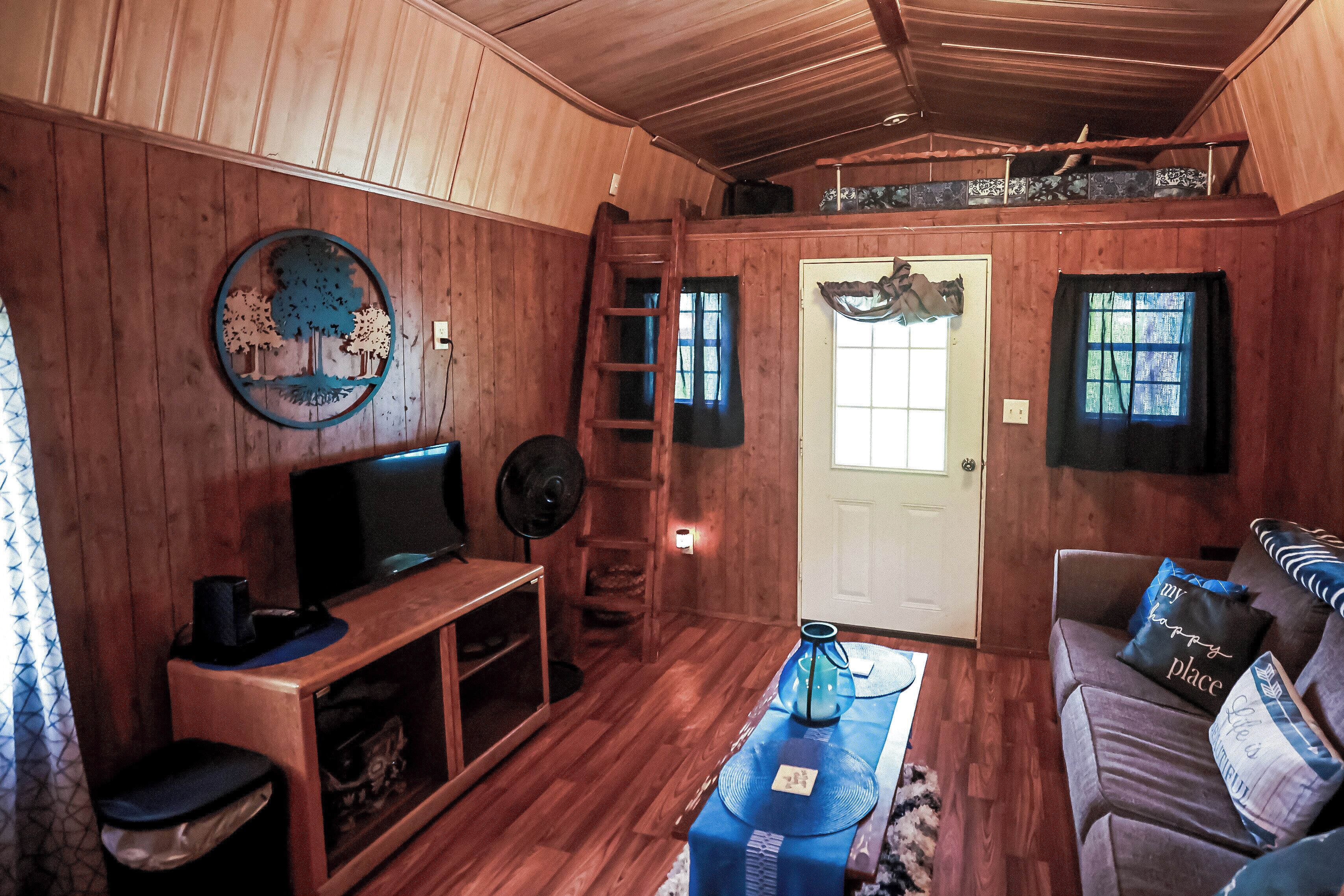 Un intérieur en bois comprenant une télévision, un canapé, une table basse, une échelle et une porte.