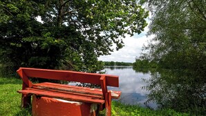 Un banco rojo junto a un río tranquilo, con abundante vegetación y árboles al fondo.