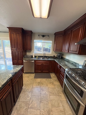 A kitchen with wooden cabinets, a stainless steel sink, a dishwasher, a stove, and a window with a view of the outdoors.