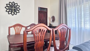 Un área de comedor con una mesa y sillas de madera, un reloj de pared decorativo, un espejo y una ventana con cortinas.