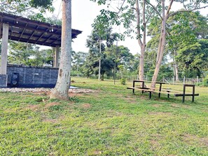 Un parc avec un banc en bois, un espace abrité équipé d’un haut-parleur et des arbres.