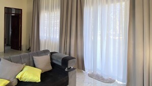 Una sala de estar con sofá, cortinas y vista por la ventana.