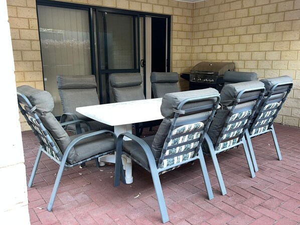 Une terrasse extérieure avec une table et des chaises, une porte-fenêtre coulissante et un barbecue.