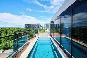 Piscina moderna en la azotea con barandillas de cristal y vistas de los edificios circundantes.