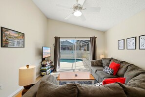 A living room with a sofa, a coffee table, a TV, and a bookshelf. - Calm & Homey 3BR Oasis with Private Pool (Davenport)