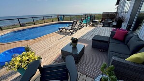 A deck with a pool, lounge chairs, a sofa, and potted plants.