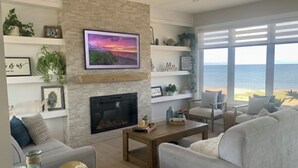 A living room with a fireplace, a large window with a view of the sea, and a cozy seating area.
