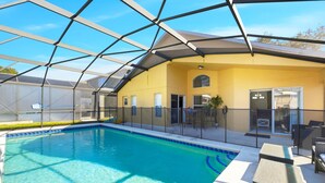 Una piscina techada con cerramiento de vidrio, un edificio amarillo con puerta y ventanas, y mobiliario exterior.