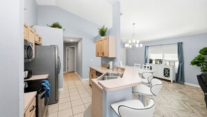 Una cocina moderna con una isla central, armarios de madera y un comedor con sillas blancas.