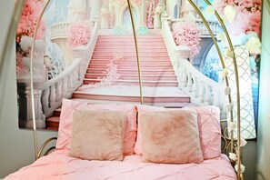 Quarto com cama com roupa de cama rosa e almofadas fofas, um arco decorativo e um mural de uma escadaria imponente com flores cor-de-rosa.